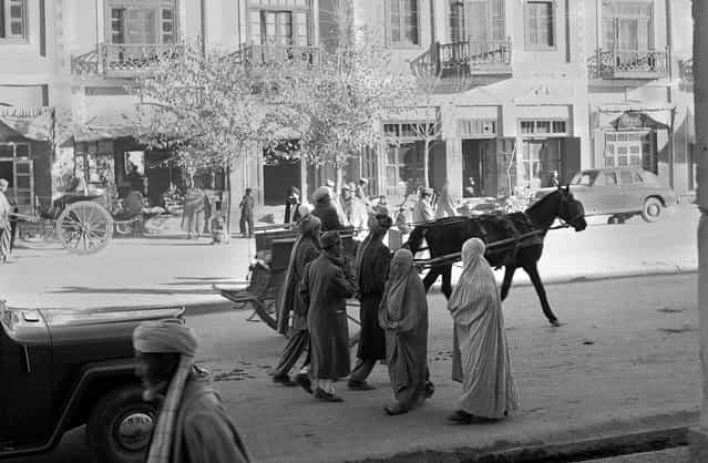 Women, wearing traditional burqas and Persian slippers, walk alongside men, cars and horse carts, in a street in Kabul, in 1951. At the time, this street was one of only three paved streets in the capital city. (Photo by AP Photo via The Atlantic)
