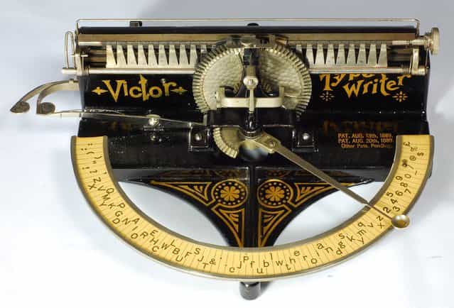 Victor index. Tilton Mfg. Co., Boston, 1889. The Victor is a beautiful Victorian typewriter with handsome decals. This was the first typewriter to use a daisy wheel, which would be a common design feature on 1980s typewriters. The daisy wheel is made of thin brass, cut with narrow radial fingers, one for each character. At the end of each finger is an embossed rubber character. To operate the Victor one puts the tip of ones index finger in the little cup at the end of the pointer, then swings the pointer up to a full 180 degrees to select the characters. The pointer is connected by a gear to the central vertical wheel that holds the daisy wheel. As the pointer swings, the daisy wheel rotates into position. A spring-loaded hammer then pushes the brass finger in the daisy wheel against the paper. This typewriter originally sold for $15.00. (Photo and caption by Martin Howard/Martin Howard Collection)