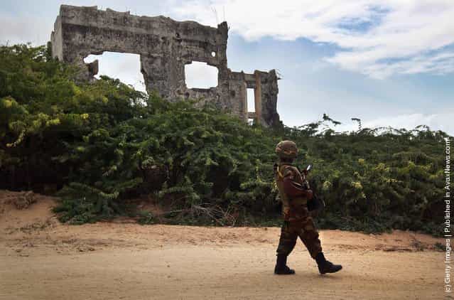 A Ugandan soldier checks his smart phone while walking past war rubble on an AMISOM base