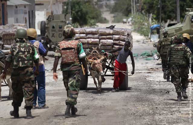 As business slowly begins anew, a laborer moves goods past Ugandan African Union soldiers in the Bakara market