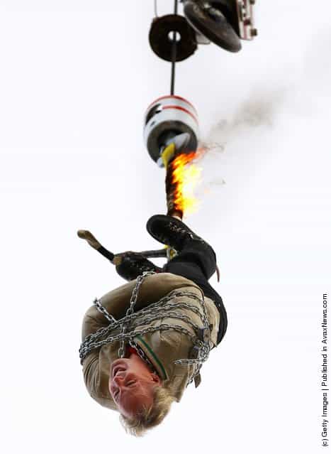 Canadian escape artist Dean Gunnarson attempts to work his way out of a straight jacket while hanging from a crane by a rope which is on fire during a Royal Melbourne Show