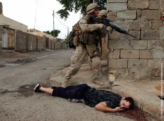 U.S. Marines from the 1st U.S. Marines Expeditionary Force pass by a dead body of a suspected insurgent during the ground offensive in Iraq