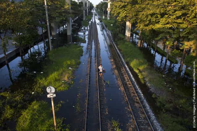 A Thai woman walks along the partially flooded train tracks in the Laksi area