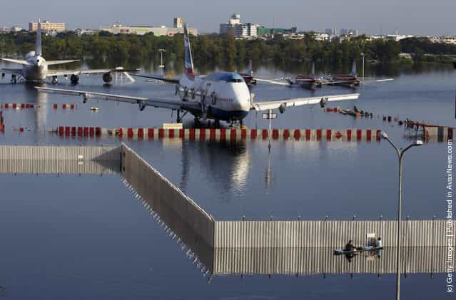 A boat paddles behind a fence near a plane sitting on the flooded tarmack of the closed Don Muang airport