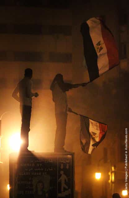 A protestor waves Egyptian flags as he stands with another on a road sign in Tahrir Square