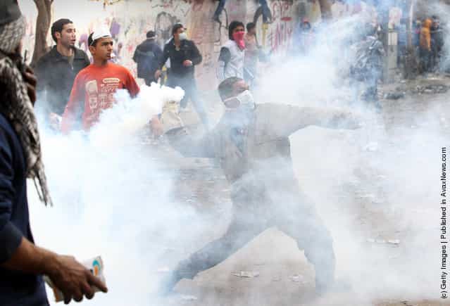 A protestor throws a tear gas canister away during clashes with police near Tahrir Square