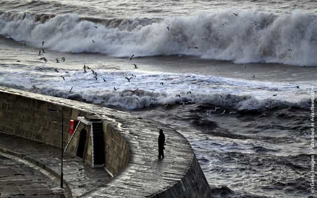 A man walks on the Cobb as storm waves break behind in Lyme Regis, England