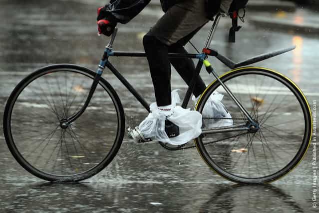 A man covers his shoes with plastic carrier bags as he cycles through the pouring rain on January in London
