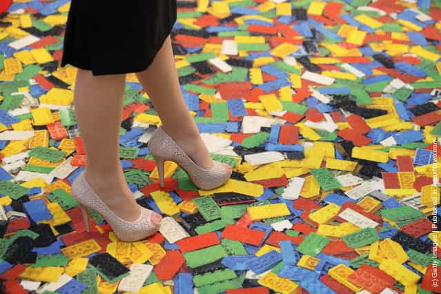 A woman stands on a carpet with a Lego brick design at the 2012 London Toy Fair