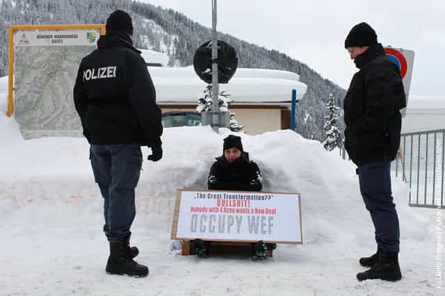 Swiss riot police men frame an Occupy protester checking personal datas in front of the main gate to Davos congress center