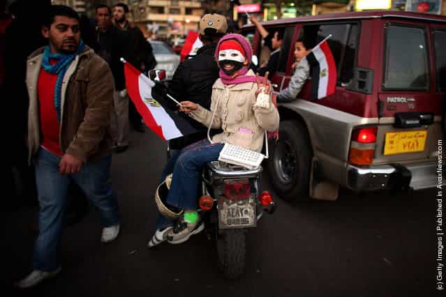 A young girl rides on the back of a motorcycle through Tahrir Square
