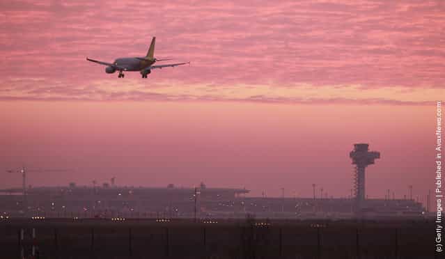 A passenger plane lands at Schoenefeld Aiport next to the construction site and the new control tower of the new Berlin Brandenburg International Aiport (BBI) at sunrise