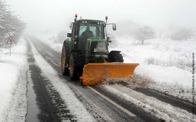 A tractor with a snow plough clears snow off the road near Dulverton