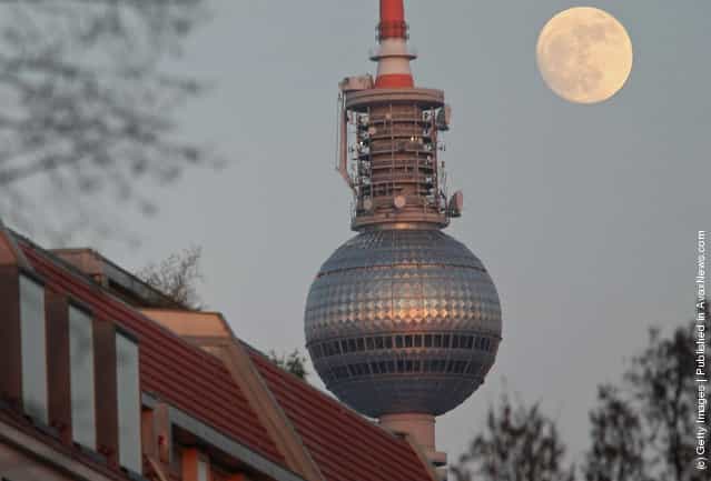 The full moon rises behind the television tower and trees with bare branches in Berlin, Germany