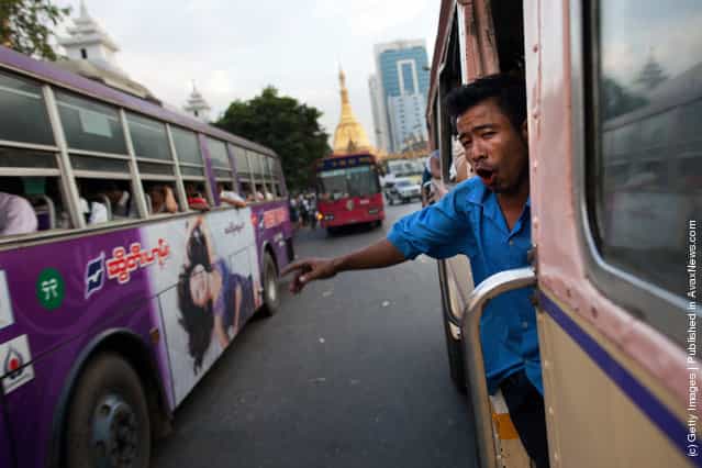 A Burmese man working on a city bus calls out for passengers to board at a bus stop in Yangon, Myanmar