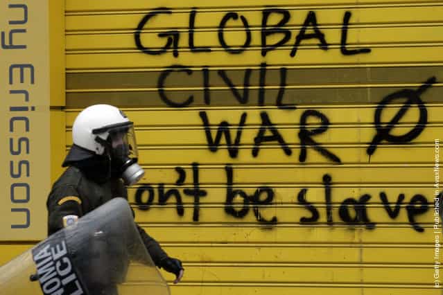A policeman walks past graffiti that says 'Global civil war, don't be slaves' during a demonstration involving thousands of civilians on February 10, 2012 in Athens, Greece