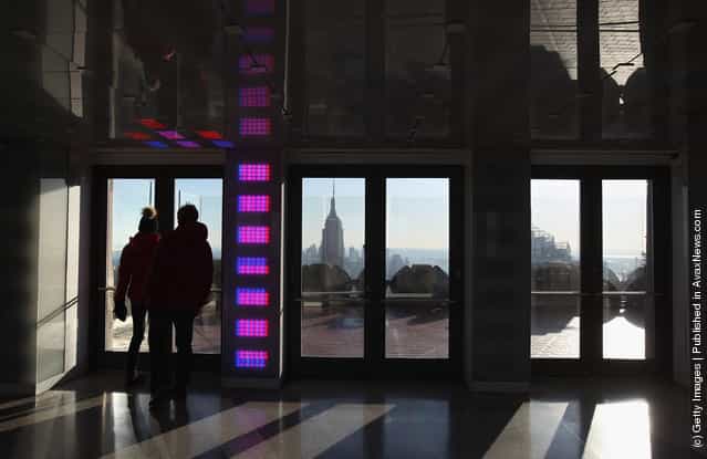Tourists walk onto an observation deck atop Rockefeller Center as the Empire State Building towers over the Manhattan skyline