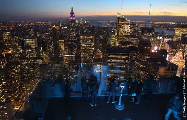 The Empire State Building towers over the Manhattan skyline as tourists gather on the observation deck of Rockefeller Center