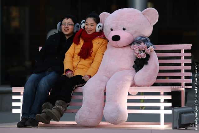 A Chinese man takes pictures with his girlfriend posing with a giant teddy bear for Valentines Day outside a shopping mall