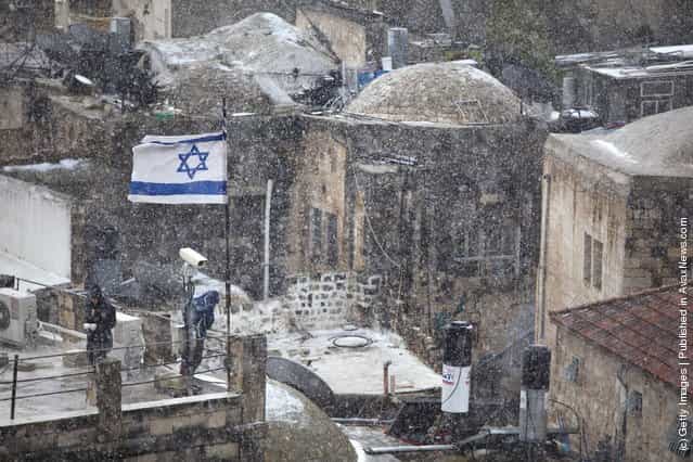 Jewish settlers stand on a rooftop as snow falls on March 2, 2012 in Jerusalem, Israel