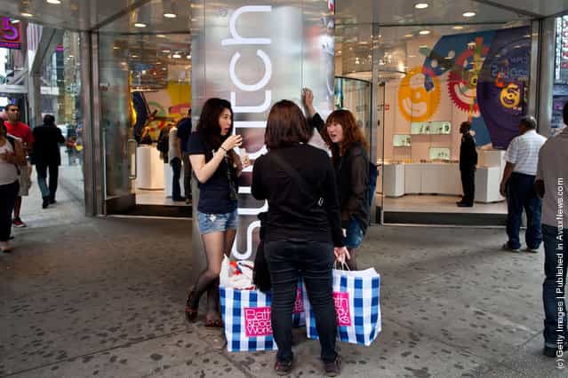 Women with shopping bags stand outside the Swatch store in Times Square