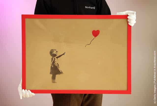 An employee holds Banksys Girl and Balloon which was painted on an Ikea frame at Bonhams auctioneers