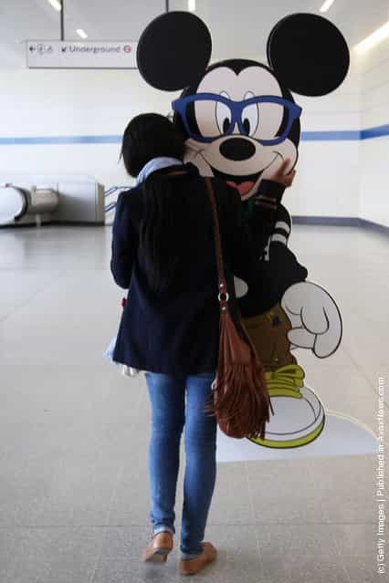 A woman carries a cardboard cut-out of Micky Mouse into Stratford Underground station