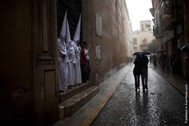 Penitents from the [La Candelaria] brotherhood find shelter from the rain as a couple walks along the street during a storm in Seville, Spain, April 3., 2012 Most of the processions were canceled in Seville due to bad weather during the Easter Holy Week