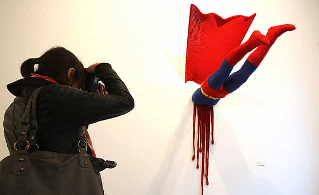 A visitor photographs the knitted sculpture [Superman] by Patricia Waller, featuring the comic book character meeting death by his own superhuman ability to fly, in the [Broken Heroes] exhibition at the Deschler Gallery in Berlin, Germany. The exhibition of hand-crocheted comic, puppet and cartoon figures shows icons of pop culture in various unfortunate states