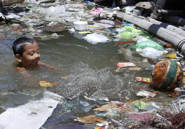 A boy swims in murky waters to cool off during a hot day outside his floating house along Manila Bay April 25, 2012