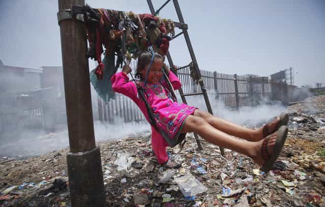 Sana, a five-year-old girl, plays on a cloth sling hanging from a signalling pole as smoke from a garbage dump rises next to a railway track in Mumbai