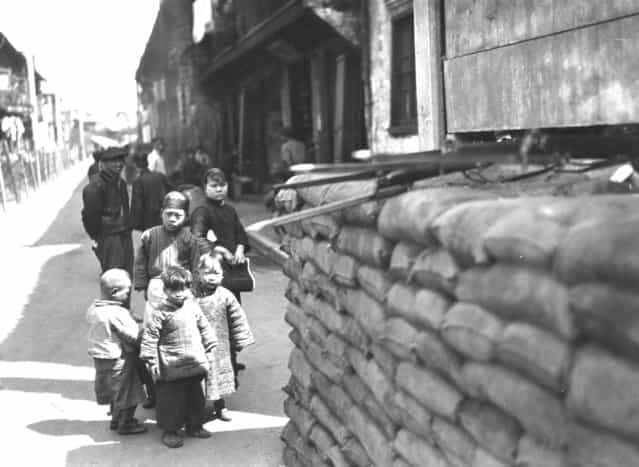 1927: Chinese children, watched over by some adults, study an artillery post. This temporary post is used to house British troops defending Shanghai