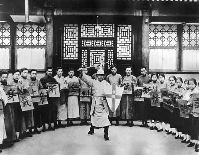 1930: Declared to be Salvation Army recruits in training for officership. They are holding up cards with Chinese symbols as they watch a sword wielding character in military uniform carrying a shield with a cross on it