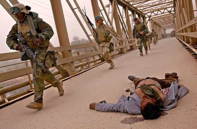 U.S. Marines of 3rd Batallion 4th Marines rush to cross the damaged Baghdad Highway Bridge, Monday, April 7, 2003, passing an Iraqi mans body, as the Marines enter the southeast outskirts of Baghdad