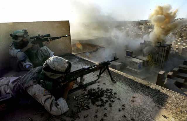 U.S. soldiers from Company C, First Battalion of the Fifth Cavalry Regiment on a rooftop in a cemetery as a round from a Bradley Fighting Vehicle hits a tomb where a sniper was suspected to be hiding, during the battle for Najaf on August 11, 2004
