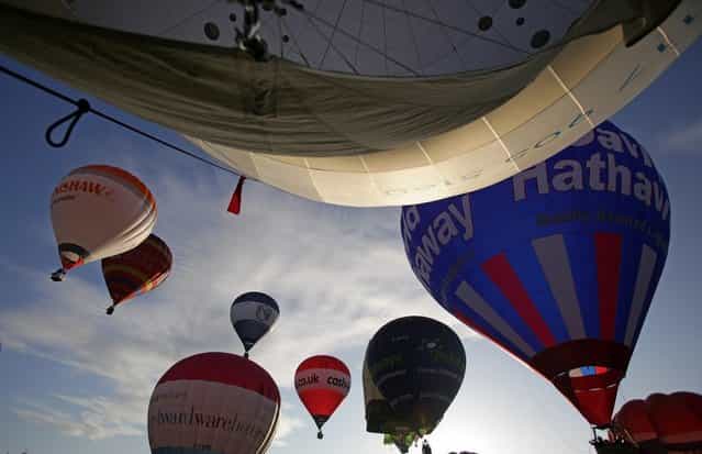 Hot air balloons take to the skies over Bristol city centre on August 6, 2012 in Bristol, England. The early morning flight of over twenty balloons over the city was organised as a curtain raiser for the four-day Bristol International Balloon Fiesta which starts on Thursday. Now in its 34th year, the Bristol International Balloon Fiesta is Europes largest annual hot air balloon event in the city that is seen by many balloonists as the home of modern ballooning. (Photo by Matt Cardy)