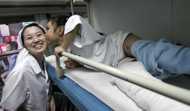 Seven-year-old Liang Kexin (R) kisses a nurse goodbye in a cabin on her way to hometown after treatment at the Wuchang Railway Station June 20, 2008 in Wuhan of Hubei Province, China. (Photo by China Photos)