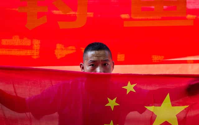 A Chinese man holds a national flag during a protest outside the Japanese Embassy in Beijing, on August 15, 2012. (Photo by Andy Wong/AP Photo)