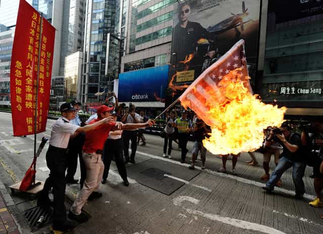 An activist waves a burning Japan-US combined flag during a demonstration over a group of disputed islands, as people make their way to the Japanese consulate in Hong Kong, on September 16, 2012. (Photo by Antony Dickson/AFP Photo)