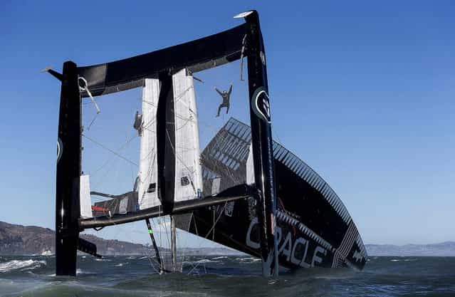 Crew members hang from mesh netting after the Oracle Team USA AC72 boat capsized in San Francisco Bay. The America's Cup champion syndicate is assessing the damage to its 72-foot catamaran after it capsized and was swept by a strong current more than four miles past the Golden Gate Bridge before rescue boats could control it. (Photo by Guilain Grenier/Oracle Team USA)