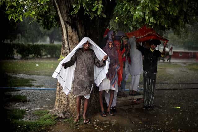 Men take shelter under a tree during a sudden downpour in New Delhi, India October 23, 2012. (Photo by Altaf Qadri/Associated Press)