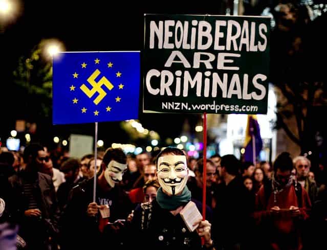 Protesters hold banners, one reading [Neoliberals are criminals] and another with an EU flag with the Nazi symbol on it during a demonstration outside Parliament as lawmakers debate budget spending cuts for 2013 in Madrid, Spain October 23, 2012. (Photo by Andres Kudacki/Associated Press)