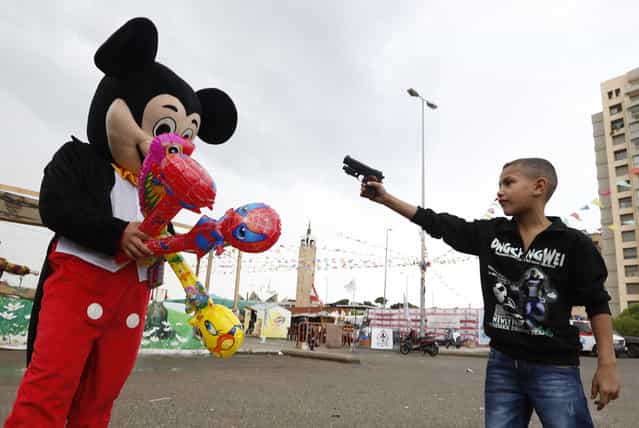 A Syrian refugee boy points a plastic toy pistol at a man in a Mickey Mouse costume on the first day of Eid al-Adha at a park in Beirut October 26, 2012. Muslims around the world celebrate Eid al-Adha, marking the end of the haj, by slaughtering sheep, goats, cows and camels to commemorate Prophet Abraham's willingness to sacrifice his son Ismail on God's command. (Photo by Jamal Saidi/Reuters)