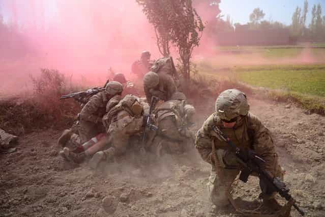 U.S. Army soldiers protect a wounded comrade from dust and smoke flares after an improvised explosive device blast during a patrol near Baraki Barak base in Logar Province, Afghanistan, on October 13, 2012. The soldier, 21-year-old Pvt. Ryan Thomas from Oklahoma, suffered soft tissue damage and after surgery in Afghanistan was scheduled to be evacuated to Germany. (Photo by Munir Uz Zaman/AFP)