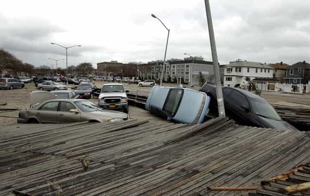 Pedestrians walk past the boardwalk and cars displaced by superstorm Sandy near Rockaway Beach in Queens, N.Y. (Photo by Frank Franklin II/Associated Press)