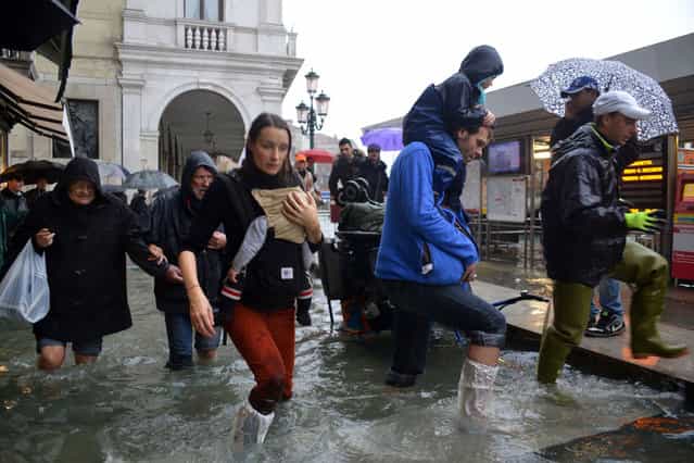 People walk in a flooded street during a 'acqua alta' on November 11, 2012 in Venice. Rain and wind hit the north of Italy on Sunday and the folooding reached 150 centimetres in Venice. (Photo by Marco Sabadin/AFP Photo)