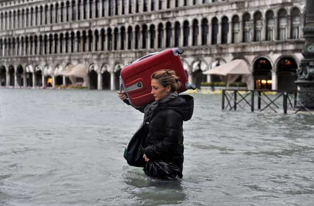 A tourist crosses flooded St. Mark's Square in Venice, Italy on November 11, 2012. Flooding is common this time of year and Sunday's level that reached a peak of 58.66 inches was below the 63 inches recorded four years ago in the worst flooding in decades. (Photo by Luigi Costantini/Associated Press)