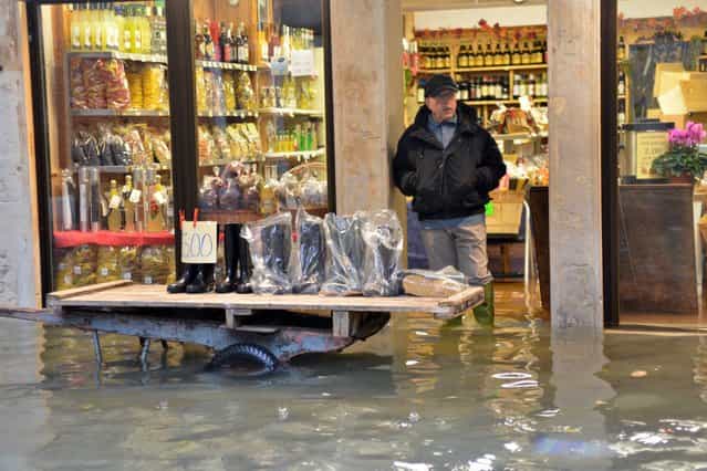 A shoes seller displays wellies outside his shop in a flooded street during a [acqua alta] on November 11, 2012 in Venice. Rain and wind hit the north of Italy on Sunday and the folooding reached 150 centimetres in Venice. (Photo by Marco Sabadin/AFP Photo)