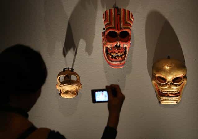 A visitor photographs Mexican, Tibetan and Cameroonian masks at the [Death: A Self-portrait] exhibition at the Wellcome Collection on November 14, 2012 in London, England. The exhibition showcases 300 works from a unique collection by Richard Harris, a former antique print dealer from Chicago, devoted to the iconography of death. The display highlights art works, historical artifacts, anatomical illustrations and ephemera from around the world and opens on November 15, 2012 until February 24, 2013. (Photo by Peter Macdiarmid)