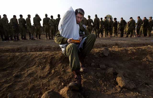 An Israeli officer holds a Torah as he reads from a holy book while others gather in a staging area near the Israel – Gaza Strip border on Monday. (Photo by Ariel Schalit/Associated Press)